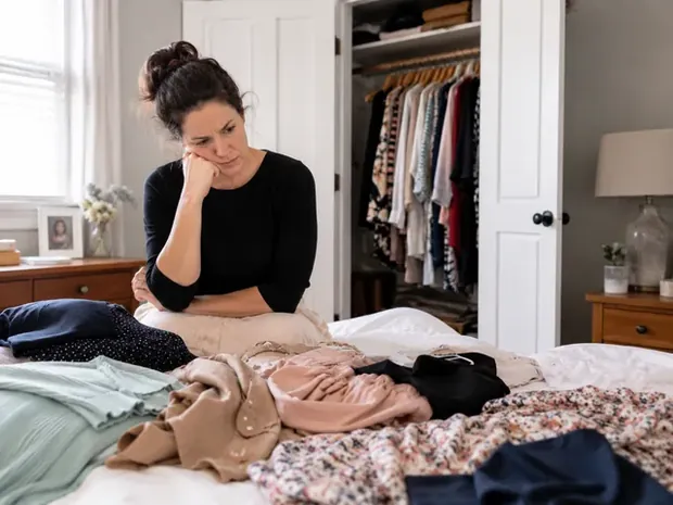 Mulher em dúvida com roupas espalhadas na cama